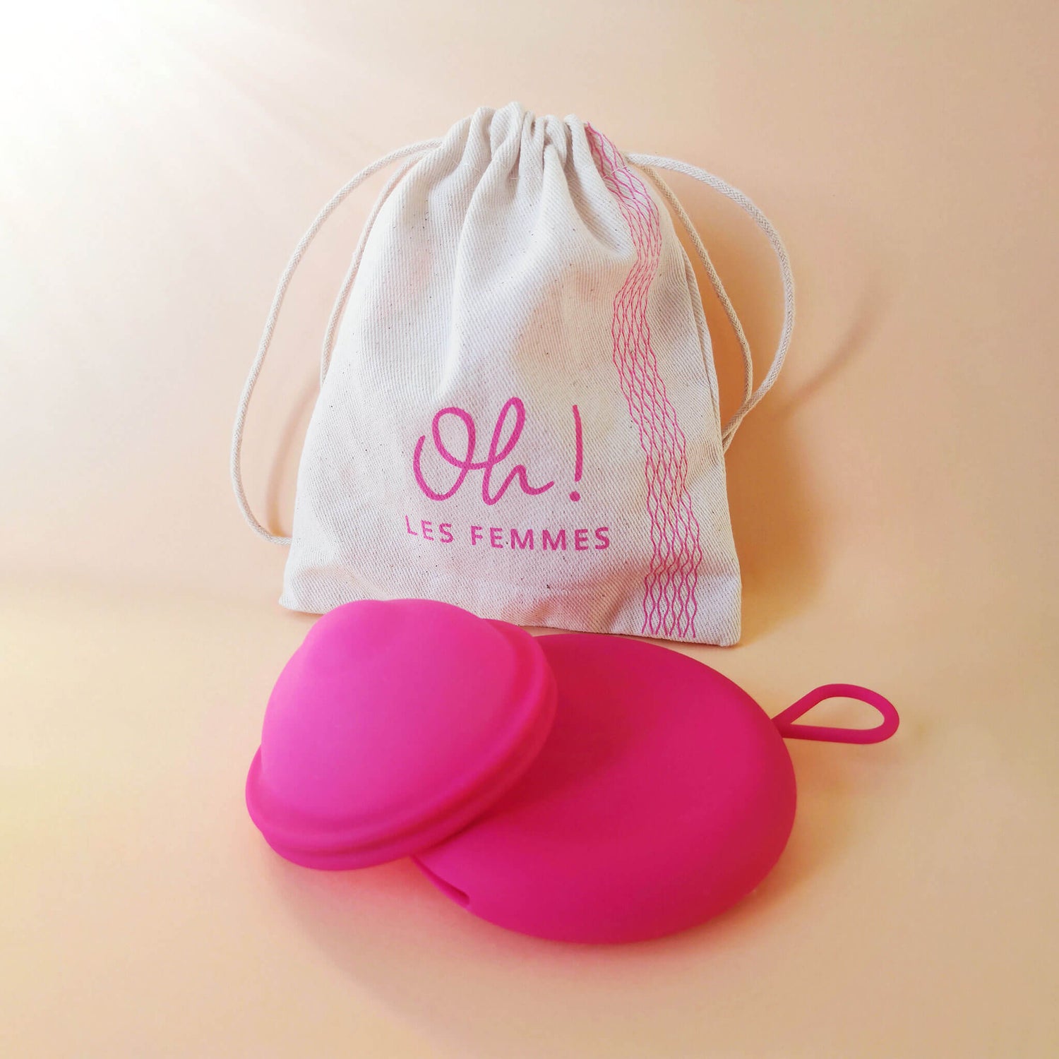 Présentation du pack : le disque menstruel discoh taille S fuchsia avec sa pochette en silicone de rangement et son pochon en coton imprimé logotisé Oh les femmes. Sur fond crème