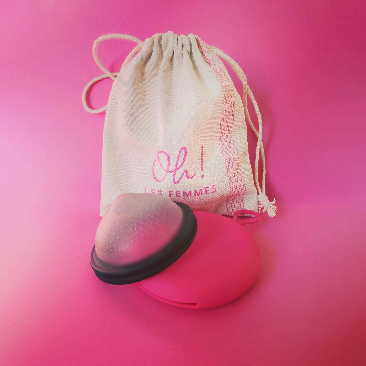 Présentation du pack : Le disque menstruel noir discoh taille L, sa pochette de rangement en silicone coloris fuchsia, avec son pochon en coton logo imprimé. Fond rose vif